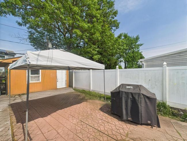 Fenced backyard featuring a detached carport, an outdoor structure, a patio area, and grilling area | Image 26