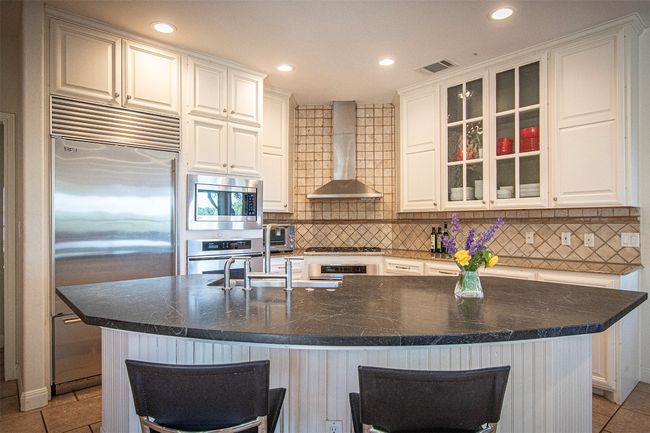 Kitchen featuring built in appliances, wall chimney range hood, white cabinetry, backsplash, and glass insert cabinets | Image 11