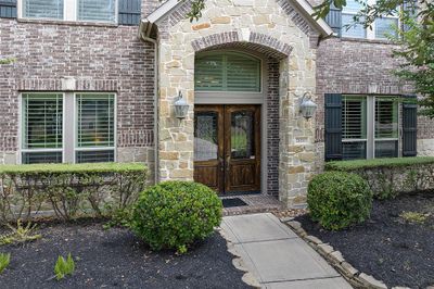 A brick and accent stone elevation, stained leaded glass double doors with a charming archway lit up by coach lighting, welcome you home! | Image 3