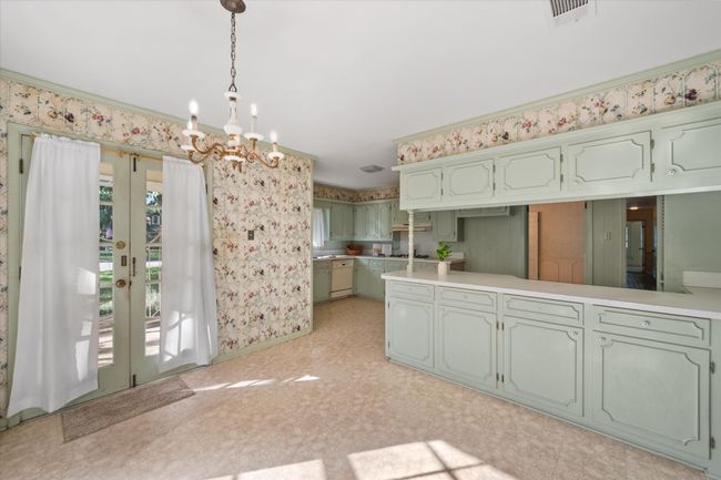 Kitchen with a chandelier, green cabinetry, decorative light fixtures, light countertops, and wallpapered walls | Image 17