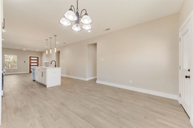 Kitchen with open floor plan, an island with sink, a chandelier, white cabinets, and pendant lighting | Image 8