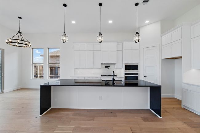 Kitchen featuring white cabinets, light wood finished floors, dark countertops, appliances with stainless steel finishes, and a sink | Image 11