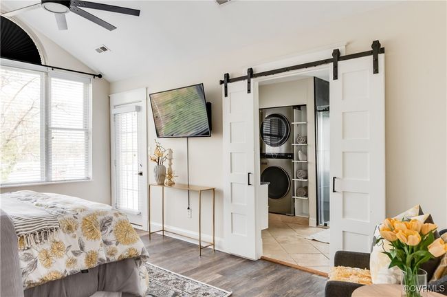 Bedroom featuring vaulted ceiling, a barn door, wood finished floors, stacked washer and clothes dryer, and visible vents | Image 35