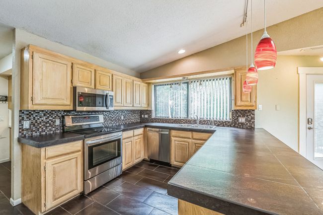 Kitchen with a sink, dark countertops, stainless steel appliances, light brown cabinetry, and vaulted ceiling | Image 14