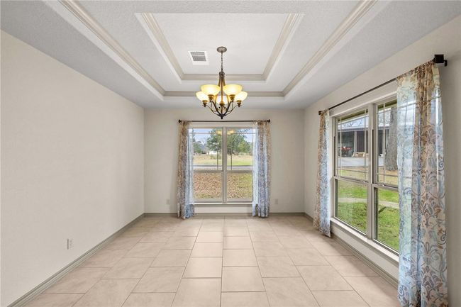 Empty room featuring a notable chandelier, light tile patterned floors, a raised ceiling, visible vents, and baseboards | Image 19