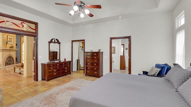 Second Primary Bedroom featuring a spacious closet, ceiling fan, light Saltillo flooring, and a raised ceiling with Wood and Glass doors and leaded glass transom window | Image 31