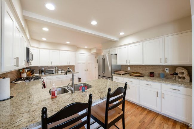 Kitchen with a peninsula, light stone counters, stainless steel appliances, decorative backsplash, and a breakfast bar area | Image 22