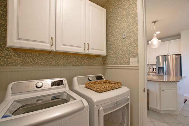 Laundry area featuring wainscoting, washing machine and dryer, cabinet space, light tile patterned floors, and wallpapered walls | Image 13
