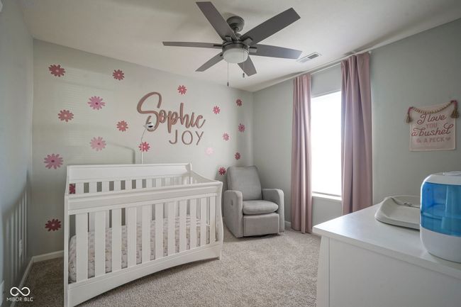 bedroom with a ceiling fan, visible vents, a nursery area, baseboards, and light colored carpet | Image 26