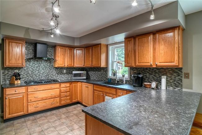 Kitchen with decorative backsplash, wall chimney range hood, kitchen peninsula, sink, and black gas stovetop | Image 17
