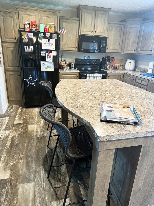 Kitchen with black appliances, crown molding, light countertops, wood finished floors, and a kitchen bar | Image 11