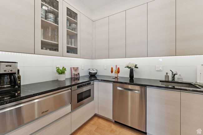 Kitchen with stainless steel dishwasher, a warming drawer, decorative backsplash, dark stone countertops, and modern cabinets | Image 19
