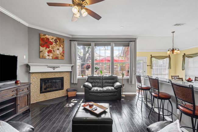 Living area with a chandelier, dark wood-type flooring, a ceiling fan, baseboards, and a glass covered fireplace | Image 5