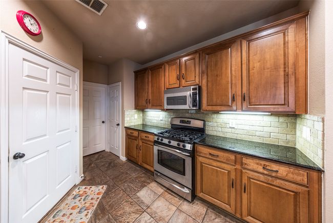 Kitchen with stainless steel appliances, brown cabinetry, tasteful backsplash, and dark stone counters | Image 13