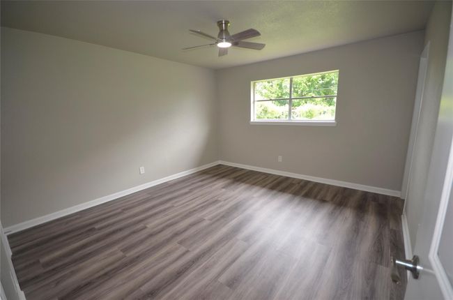 This primary bedroom is bright and spacious with modern wood-style flooring, neutral walls, a ceiling fan, and a large window offering plenty of natural light. Ideal for a restful retreat! | Image 18