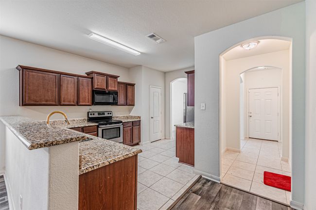 Kitchen featuring stainless steel range with electric cooktop, black microwave, light stone counters, light tile patterned flooring, and a peninsula | Image 10