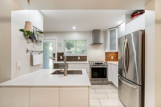 Kitchen with wall chimney range hood, appliances with stainless steel finishes, a sink, a peninsula, and light tile patterned floors | Image 4