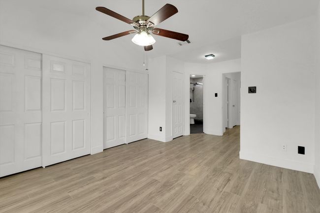 Unfurnished bedroom with two closets, light wood finished floors, a ceiling fan, and ensuite bath | Image 11