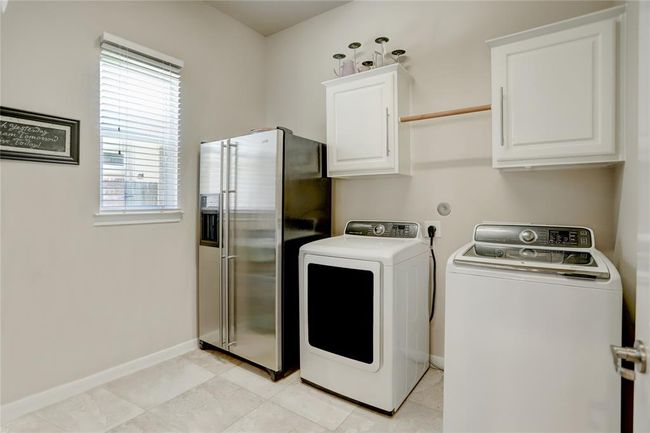 The laundry room is notably spacious, including room for side-by-side, full-sized washer and dryer as well as room for a large side-by-side refrigerator. Above the washer and dryer are white storage cabinets and a closet rod for hang drying. Not pictured is a wall-mounted table for sorting and folding clothes. | Image 25