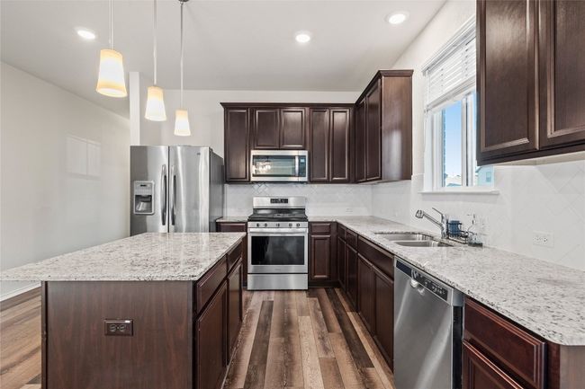Kitchen with pendant lighting, dark hardwood / wood-style flooring, sink, a kitchen island, and stainless steel appliances | Image 16