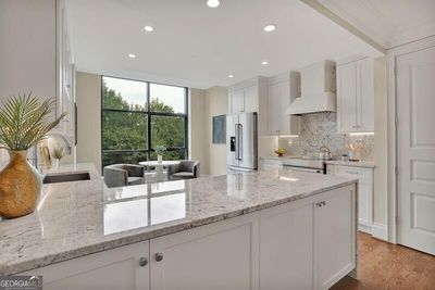 Kitchen featuring white cabinets, custom exhaust hood, appliances with stainless steel finishes, hardwood / wood-style flooring, and sink | Image 2