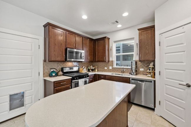 Kitchen with a center island, decorative backsplash, a sink, visible vents, and appliances with stainless steel finishes | Image 8