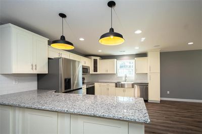 Kitchen with stainless steel appliances, dark wood-type flooring, kitchen peninsula, hanging light fixtures, and sink | Image 1