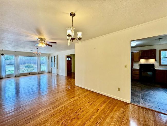 Empty room featuring a chandelier, wood finished floors, a ceiling fan, ornamental molding, and a textured ceiling | Image 6