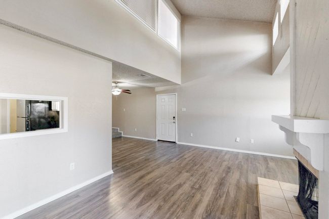 Unfurnished living room with wood finished floors, baseboards, a ceiling fan, a fireplace, and a towering ceiling | Image 13