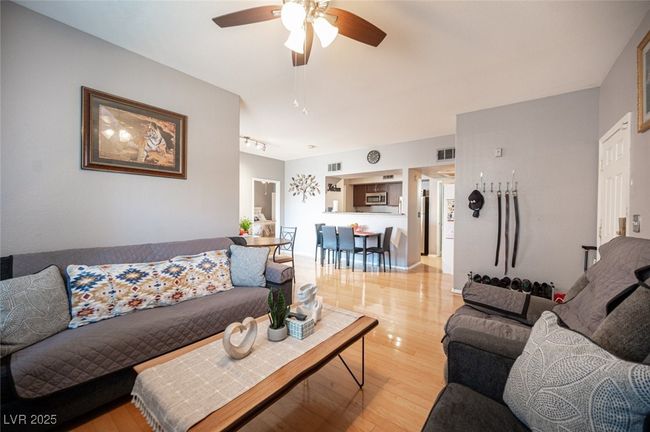 Living area featuring light wood-type flooring, rail lighting, a ceiling fan, and visible vents | Image 6