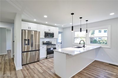 Kitchen featuring stainless steel appliances, sink, pendant lighting, white cabinets, and quartz counters | Image 3