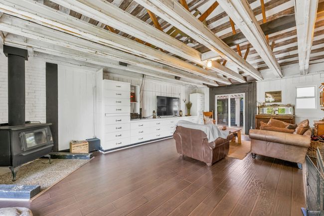 Living area with beamed ceiling, wood walls, dark wood-type flooring, and a wood stove | Image 17
