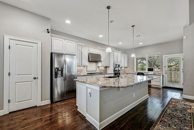 Kitchen featuring appliances with stainless steel finishes, under cabinet range hood, tasteful backsplash, dark wood-type flooring, and recessed lighting | Image 10