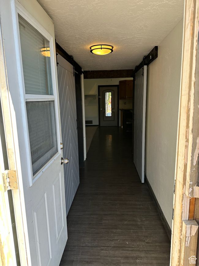 Hallway with a barn door, dark wood-type flooring, and a textured ceiling | Image 12