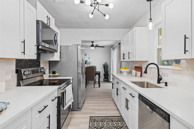 Kitchen featuring stainless steel appliances, light countertops, a sink, and white cabinetry | Image 13