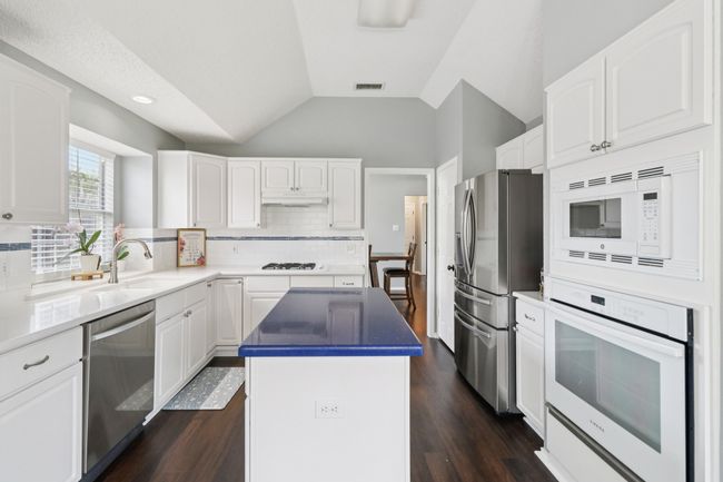 Kitchen with stainless steel appliances, a sink, a kitchen island, under cabinet range hood, and tasteful backsplash | Image 12