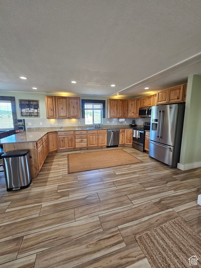 Kitchen featuring stainless steel appliances, granite countertops, a bar, decorative backsplash, and beautiful flooring | Image 31