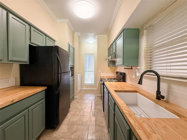 Kitchen featuring green cabinets, butcher block counters, crown molding, black appliances, and decorative backsplash | Image 7