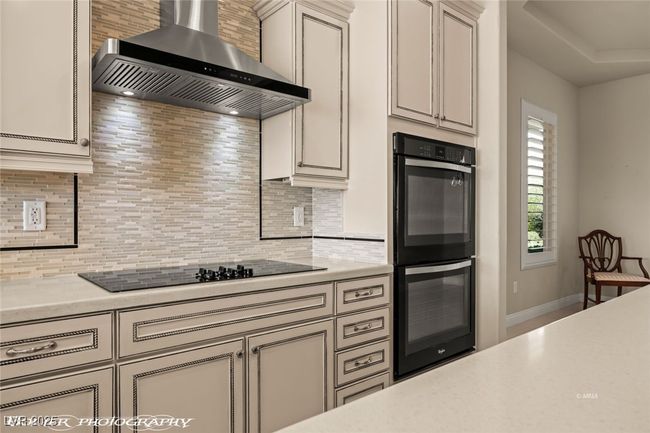 Kitchen featuring light countertops, tasteful backsplash, wall chimney range hood, and black appliances | Image 19