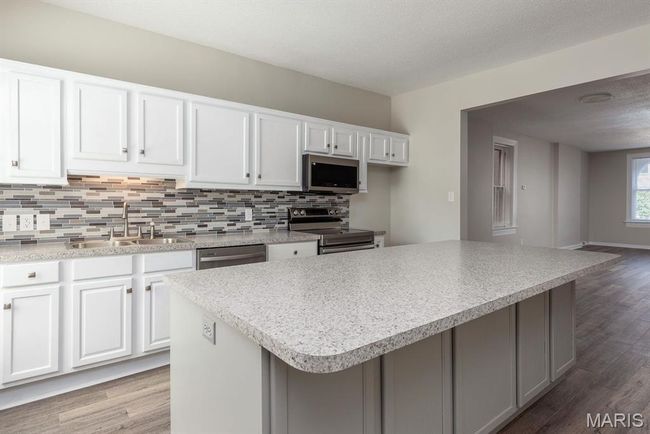 Kitchen with stainless steel appliances, tasteful backsplash, wood finished floors, white cabinets, and light countertops | Image 8