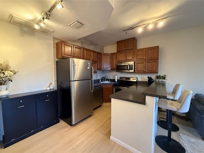 Kitchen featuring stainless steel appliances, a peninsula, light wood-style floors, a kitchen breakfast bar, and dark countertops | Image 23