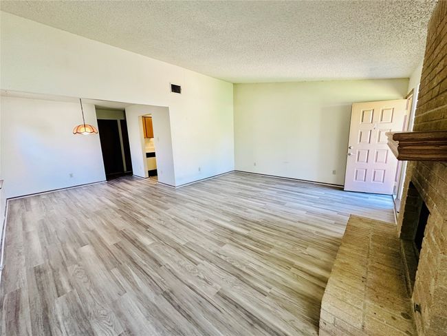 Unfurnished living room with light wood-type flooring, a brick fireplace, and a textured ceiling | Image 7