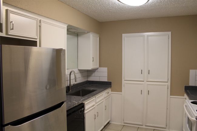 Kitchen with freestanding refrigerator, black dishwasher, wainscoting, a textured ceiling, and white cabinetry | Image 5