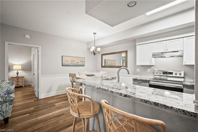 Kitchen with light stone counters, under cabinet range hood, stainless steel electric range, and a kitchen breakfast bar | Image 23