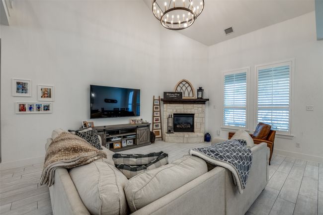 Living area featuring high vaulted ceiling, wood tiled floor, an inviting chandelier, baseboards, and visible vents | Image 6