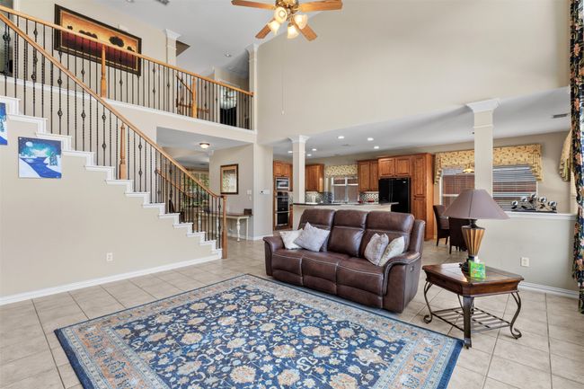 Living area featuring ornate columns, a ceiling fan, light tile patterned floors, baseboards, and a towering ceiling | Image 14