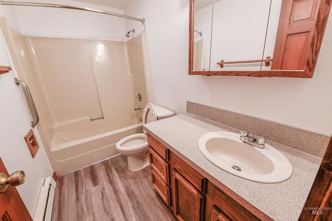 Full bathroom featuring a baseboard heating unit, wood finished floors, vanity, and shower / bath combination | Image 5