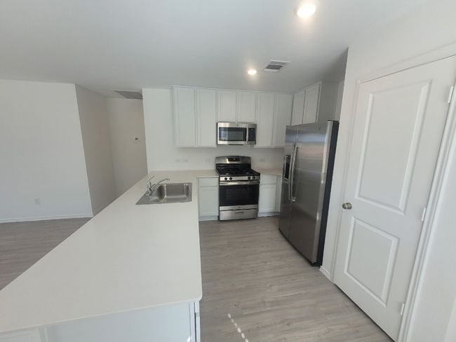 Kitchen with appliances with stainless steel finishes, a peninsula, light wood vinyl finished floors, light countertops | Image 7
