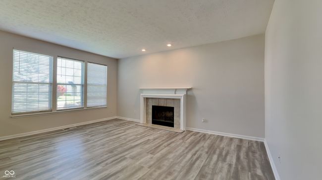 unfurnished living room featuring wood finished floors, a textured ceiling, a fireplace, recessed lighting, and baseboards | Image 6