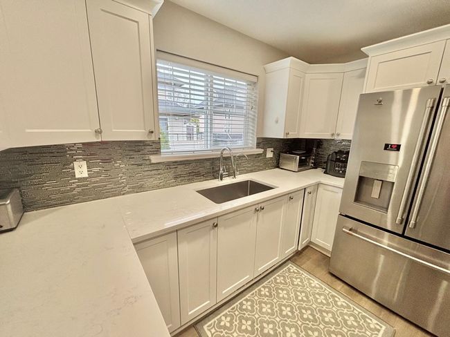 Kitchen featuring stainless steel fridge, white cabinetry, tasteful backsplash, light stone countertops, and light wood finished floors | Image 8